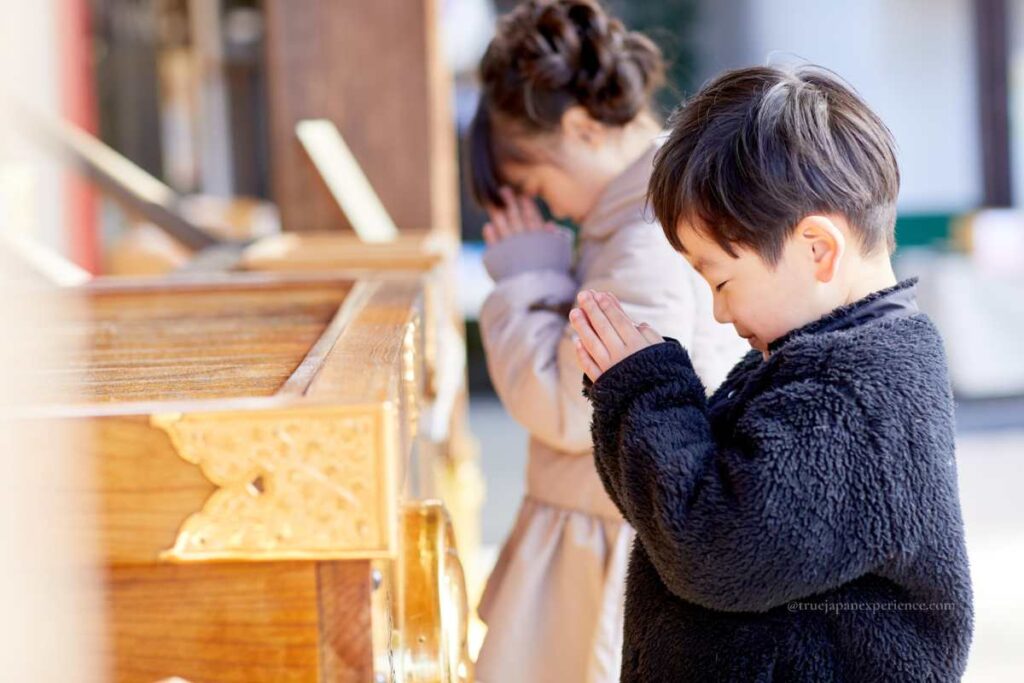 Children praying at a Shinto shrine in front of a saisen box, showing traditional Japanese worship manners