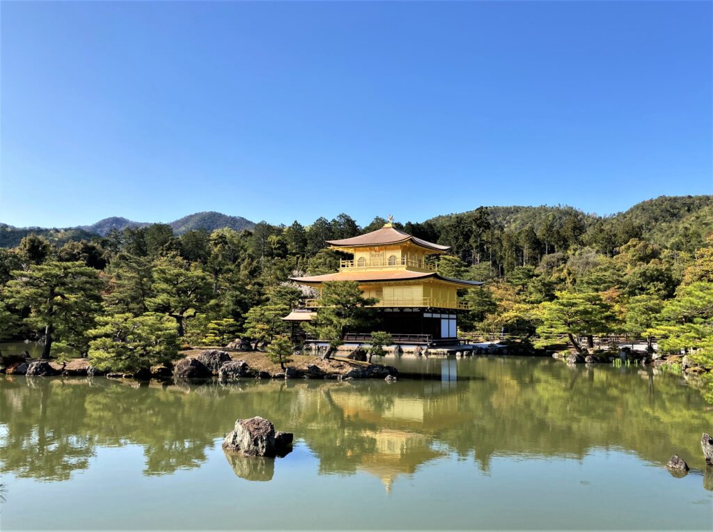 Distant view of Kinkaku-ji reflecting on the pond, surrounded by lush greenery and mountains
