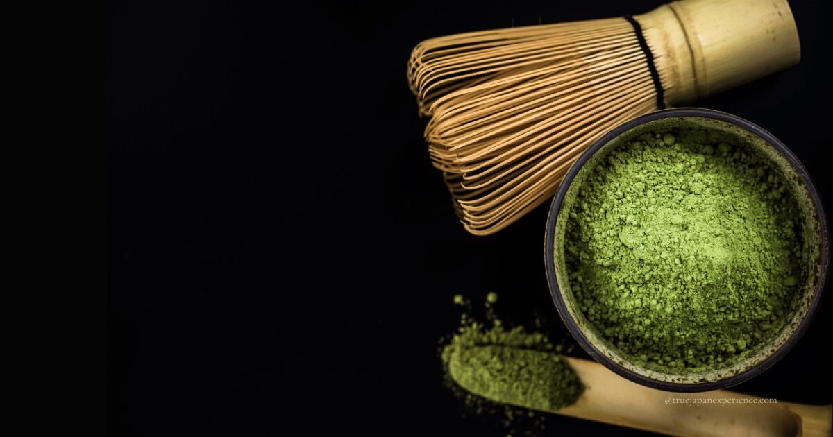 Matcha powder in a ceramic bowl with a bamboo tea whisk (chasen) and scoop (chashaku) on a black background, representing traditional Japanese tea ceremony tools