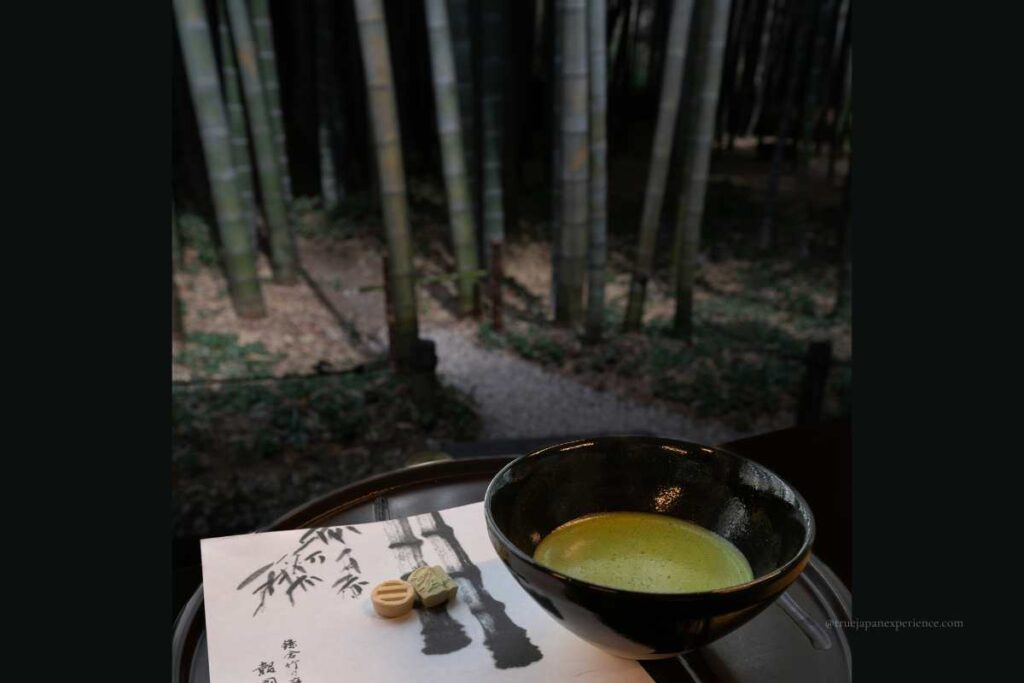 A bowl of matcha and traditional Japanese sweets placed on a tray, with a view of a bamboo forest garden in the background.