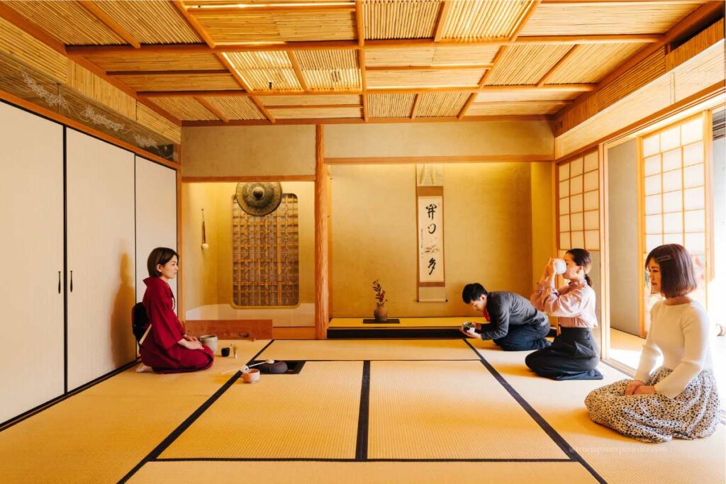 A Japanese tea ceremony in a traditional tatami room, with a kimono-clad host and guests respectfully drinking matcha and observing tea etiquette.