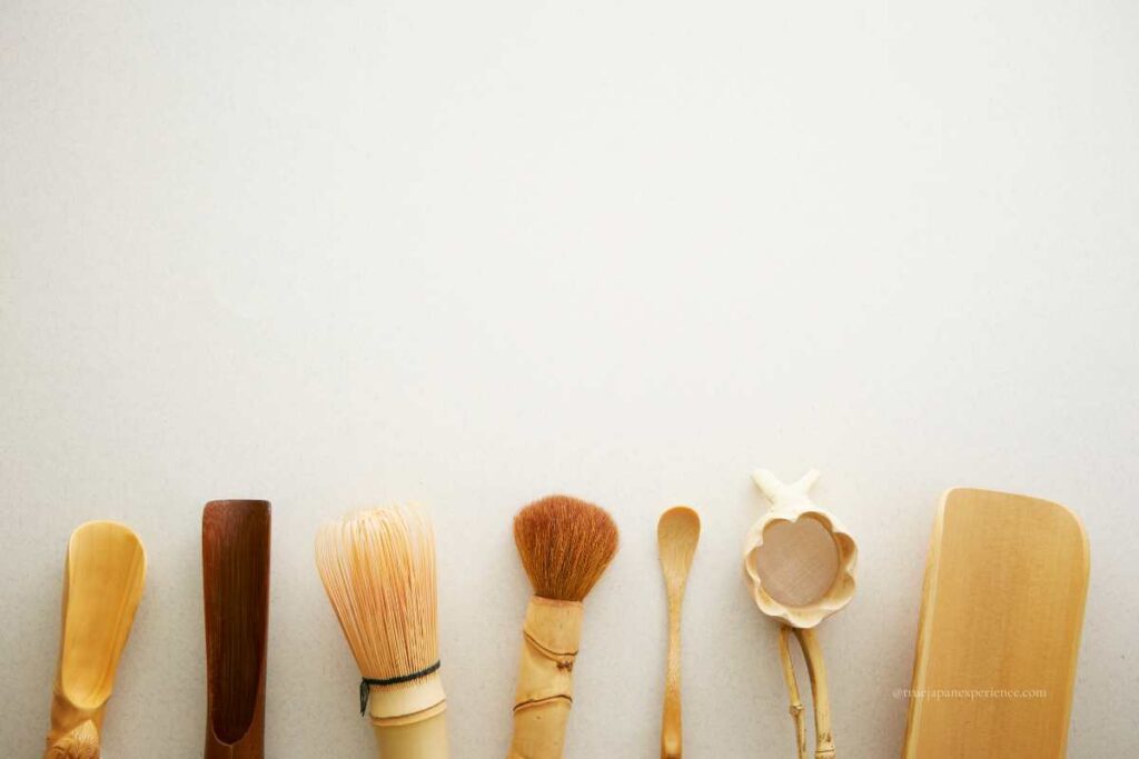 A row of traditional Japanese tea ceremony utensils, including bamboo scoops, whisks, brushes, and a tea strainer, displayed on a white background.