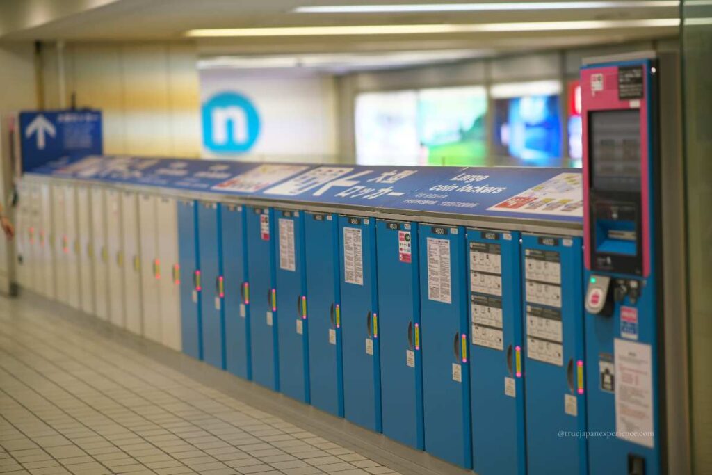 A row of large coin lockers in a Japanese train station, with blue and white doors and a touch-screen payment system.
