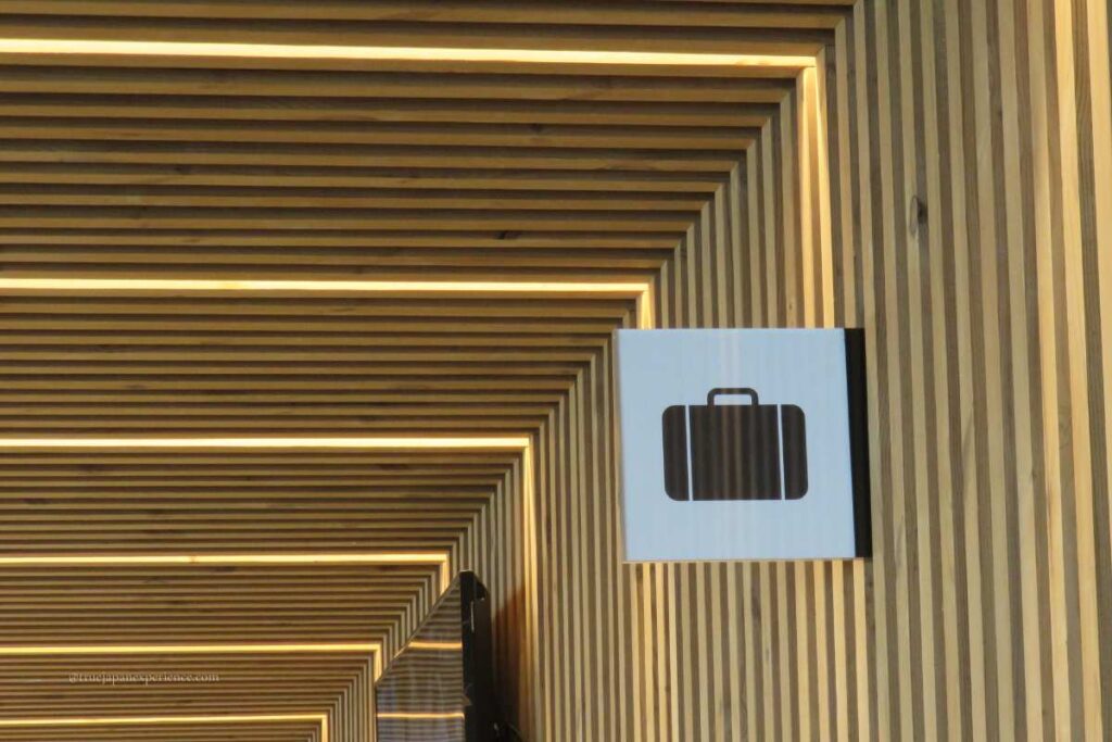 A suitcase icon sign indicating a luggage storage area, mounted on a wooden wall with geometric lighting.