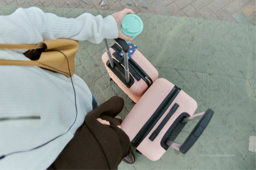 Traveler holding two pink suitcases and a drink, viewed from above.