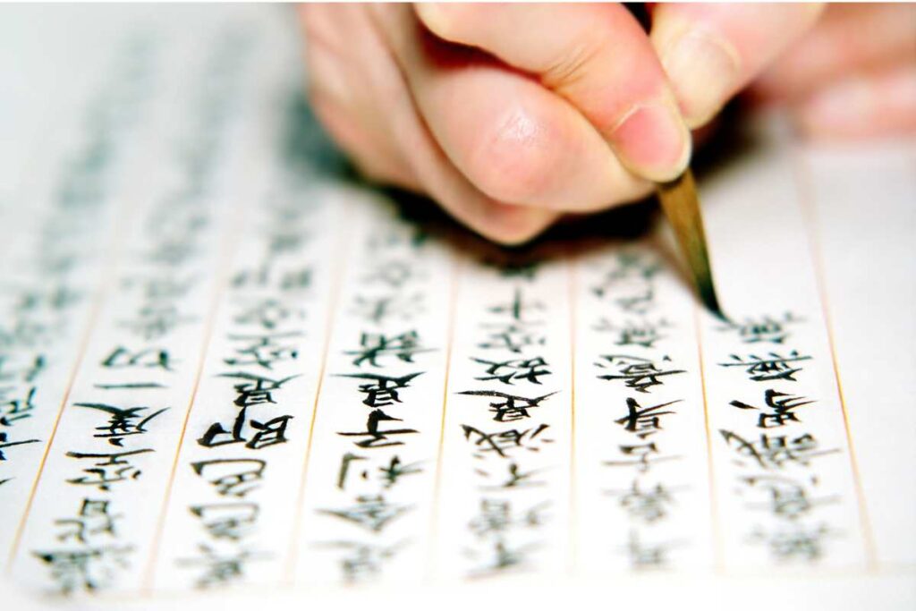 A close-up of a person copying Buddhist sutras by hand with a brush. This traditional practice is the origin of Goshuin.