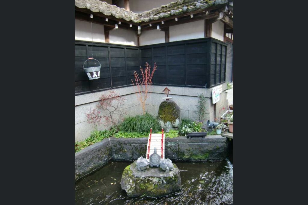 A small garden scene with flowing water, turtles, a red bridge, and a stone spring marking the site of Sogi-sui in Gujo Hachiman.