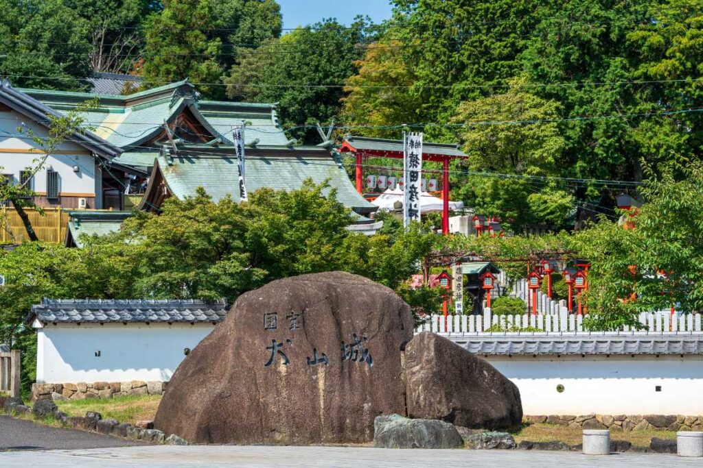 Stone monument marking Inuyama Castle, with a shrine and red torii gates in the background