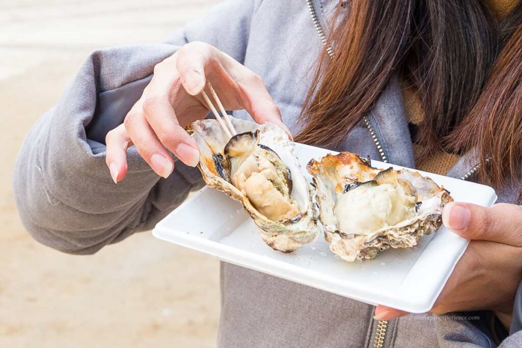 Grilled oysters on a plate held by a woman on Miyajima Island, Hiroshima