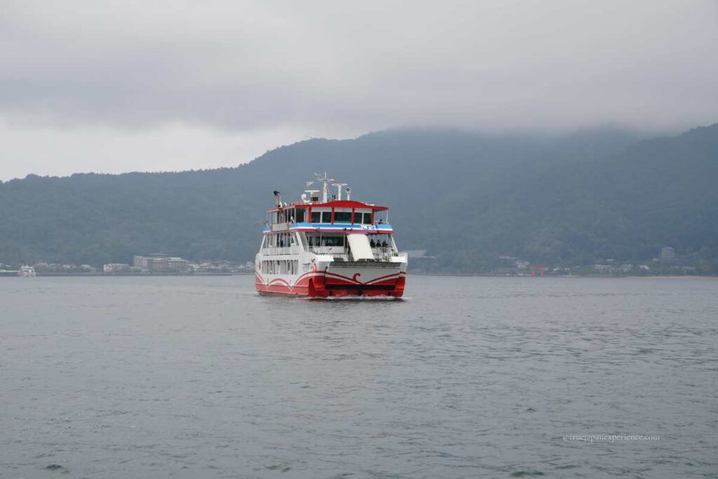 A ferry boat approaching Miyajima Island on a cloudy day, with the floating torii gate of Itsukushima Shrine visible in the distance