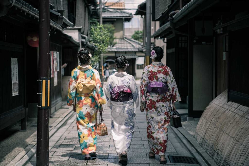 Three people in kimono walking down a quiet traditional alleyway in Japan