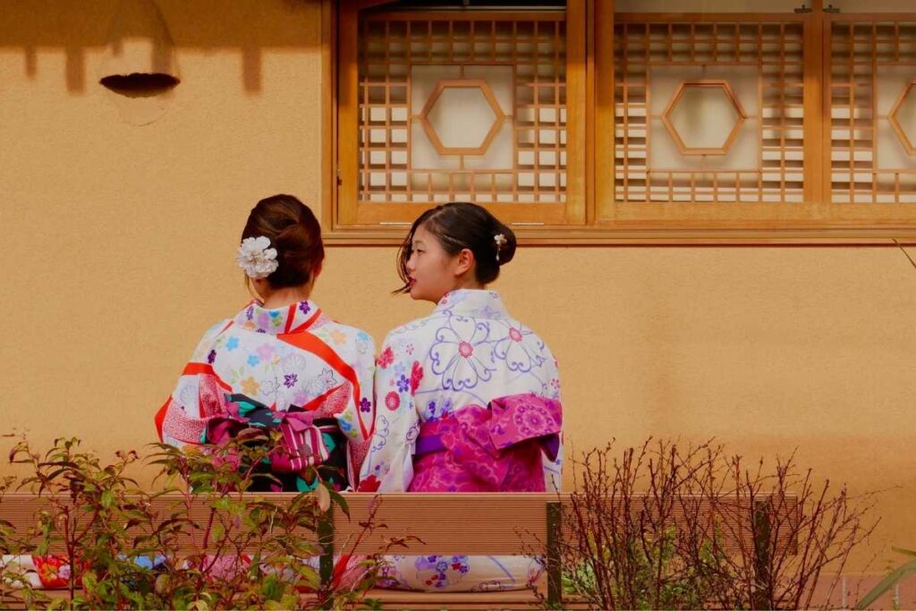 Two women in kimono sitting on a bench, enjoying a quiet moment in a traditional Japanese setting