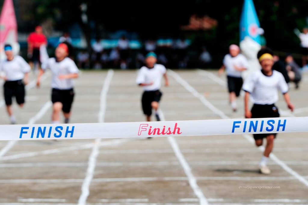 Children running toward the finish line during a school sports day race in Japan, symbolizing the energy of autumn activities.