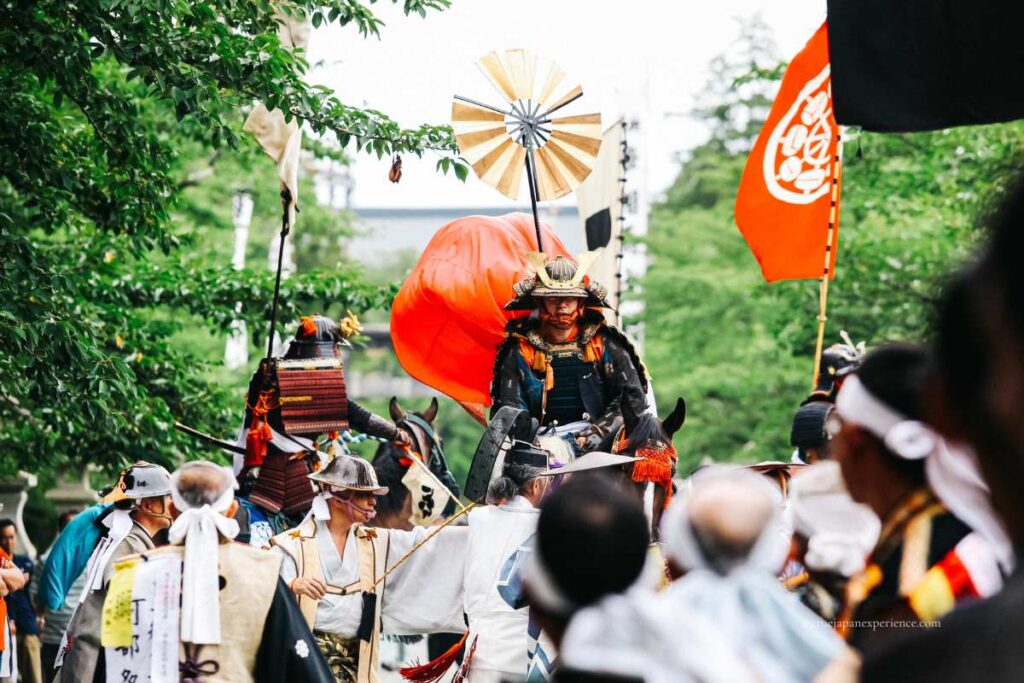 Samurai in traditional armor riding a horse during a historical festival parade in Japan, surrounded by participants in period costumes.