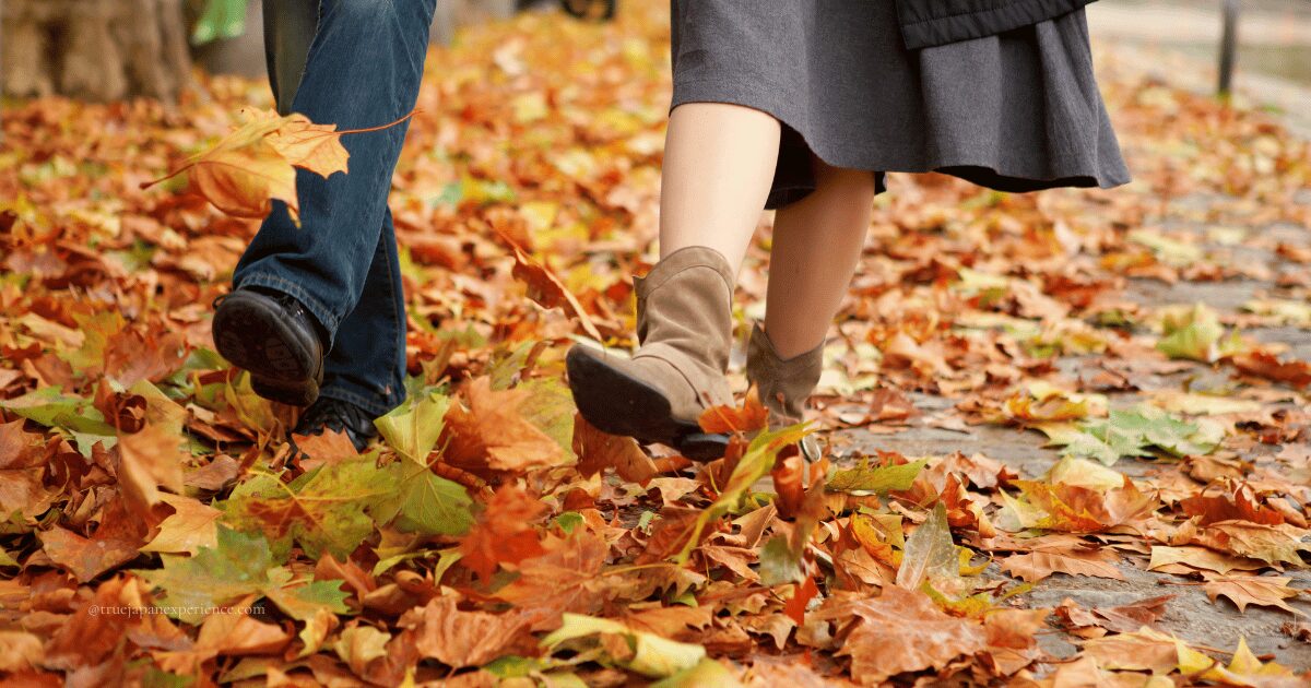 A man and woman walking through fallen autumn leaves, wearing seasonal clothes and boots