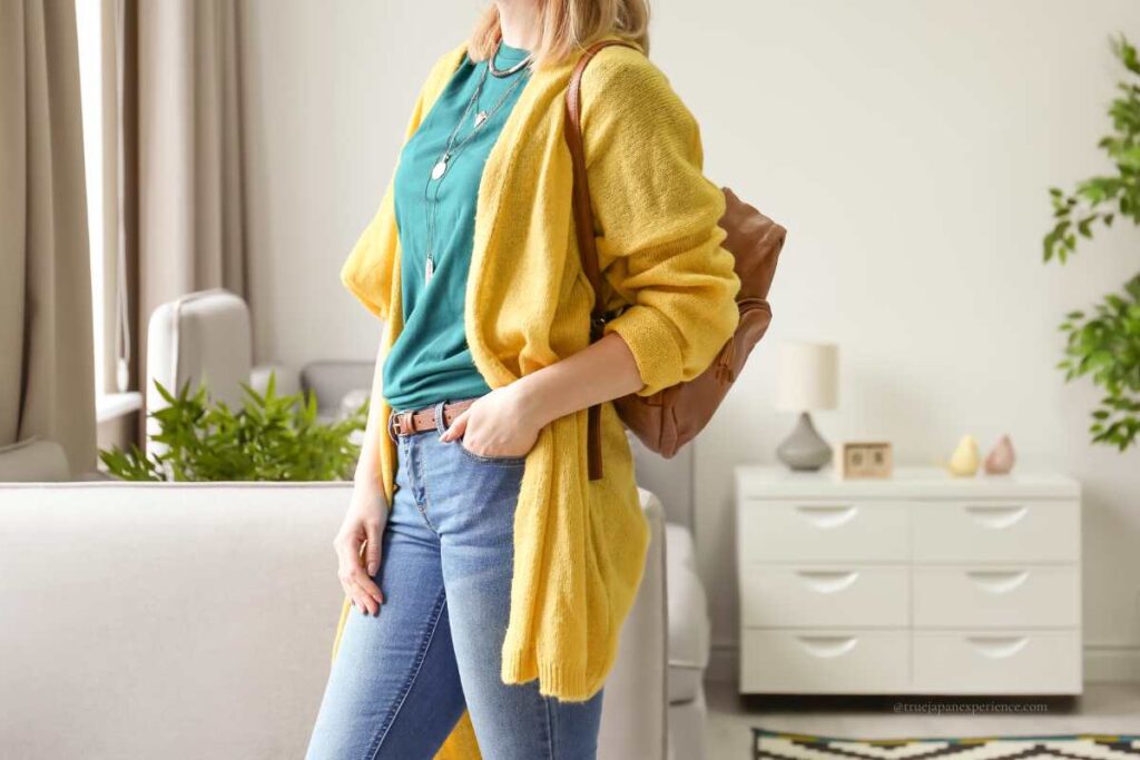 A woman wearing a yellow cardigan and jeans, standing indoors with a backpack