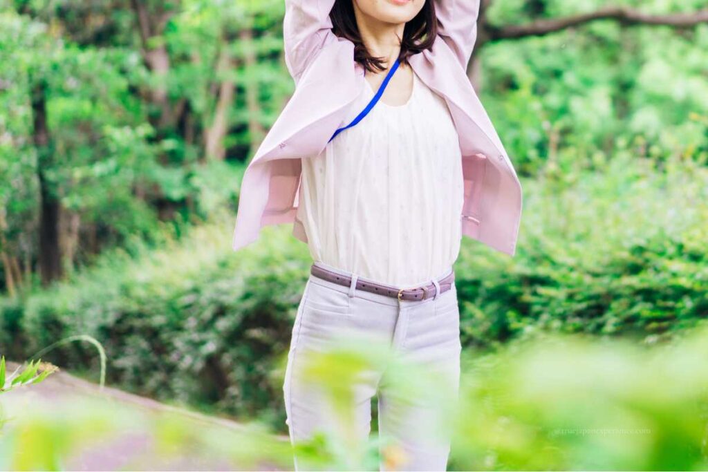 A woman stretching outdoors, wearing a pale jacket and trousers