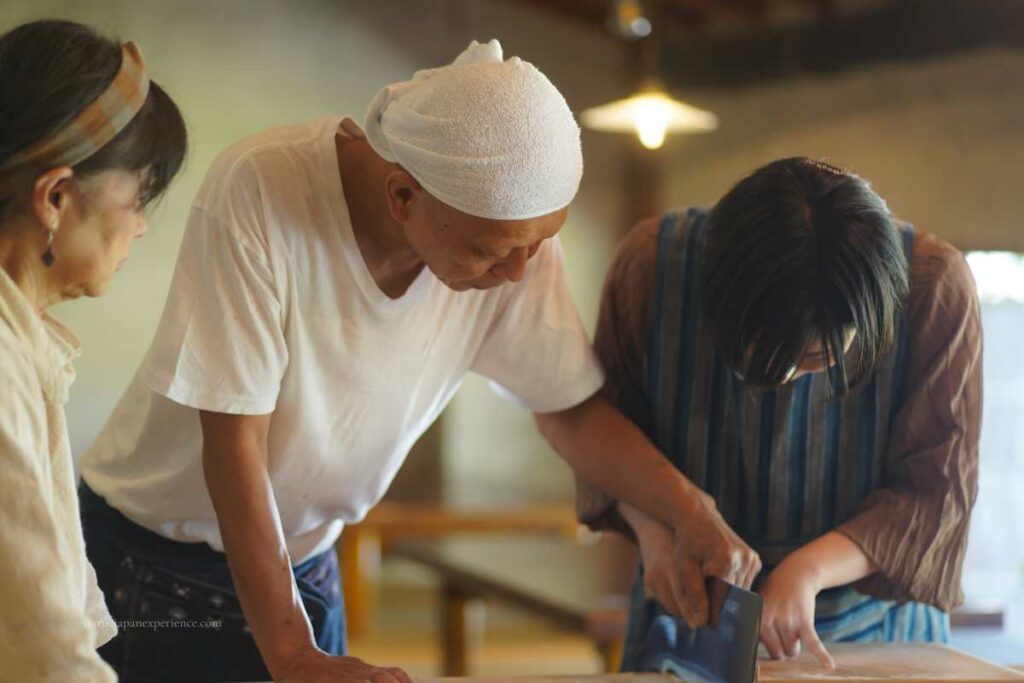 A Japanese cooking instructor helps a student cut handmade noodles during a traditional food experience.