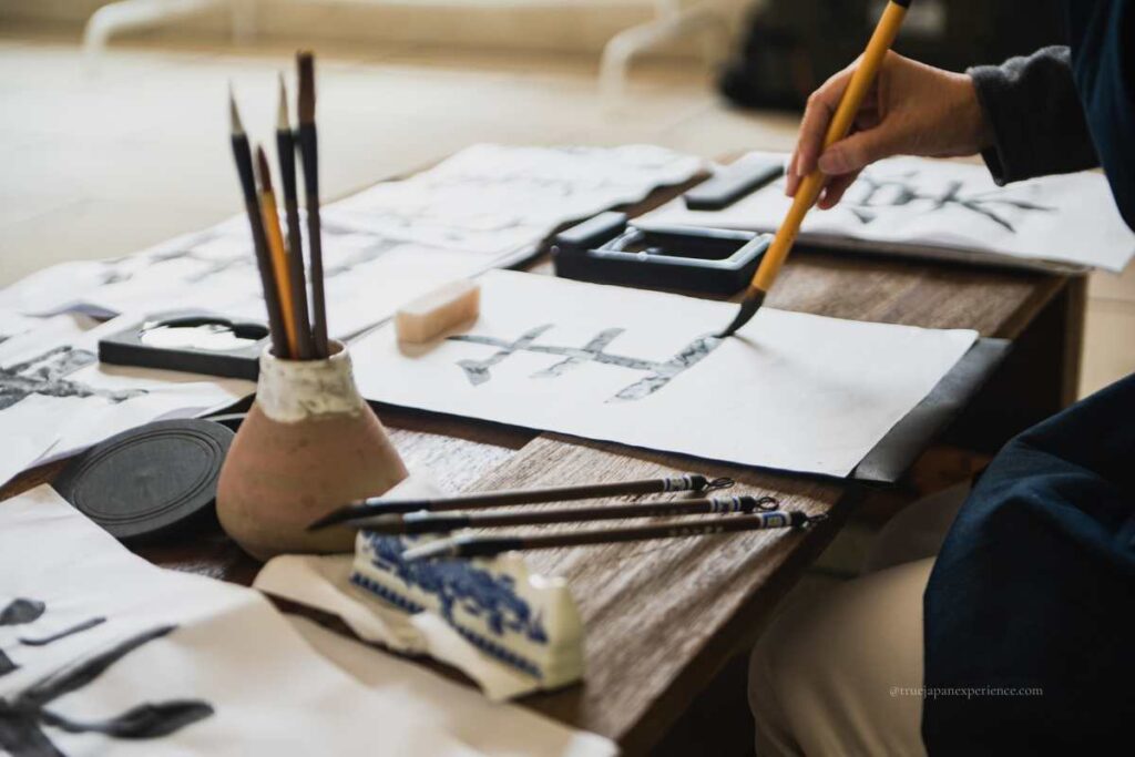 A person practicing Japanese calligraphy with brush and ink on a low table