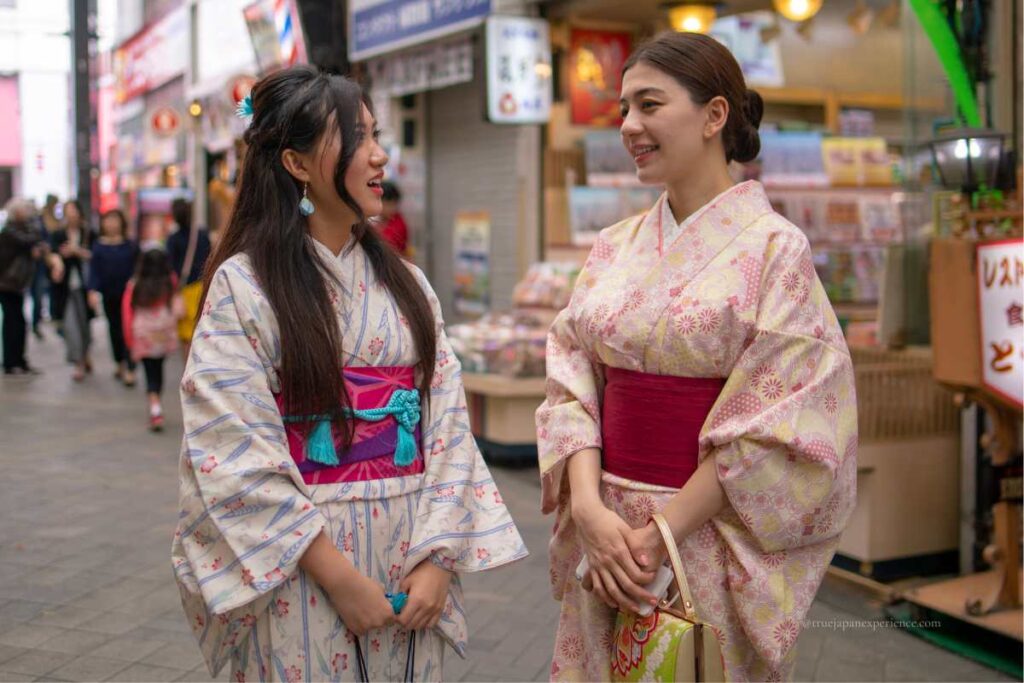 Two women in colorful kimono smiling and chatting on a shopping street in Asakusa, Tokyo.