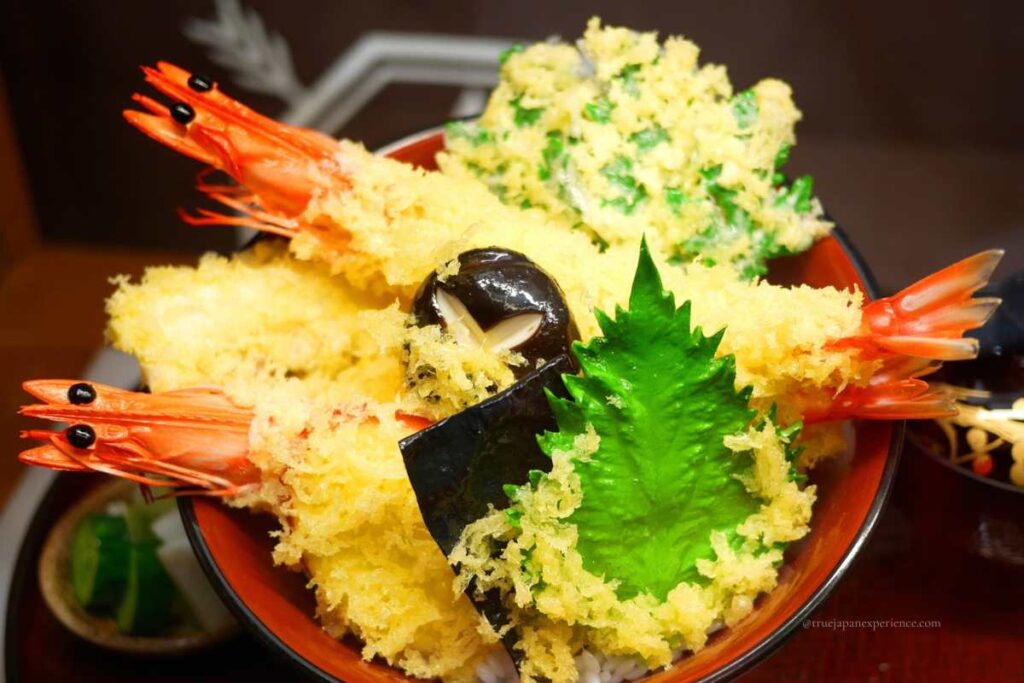 A hyper-realistic food sample of tempura rice bowl (tendon) with shrimp, vegetables, and seaweed, displayed in Asakusa.