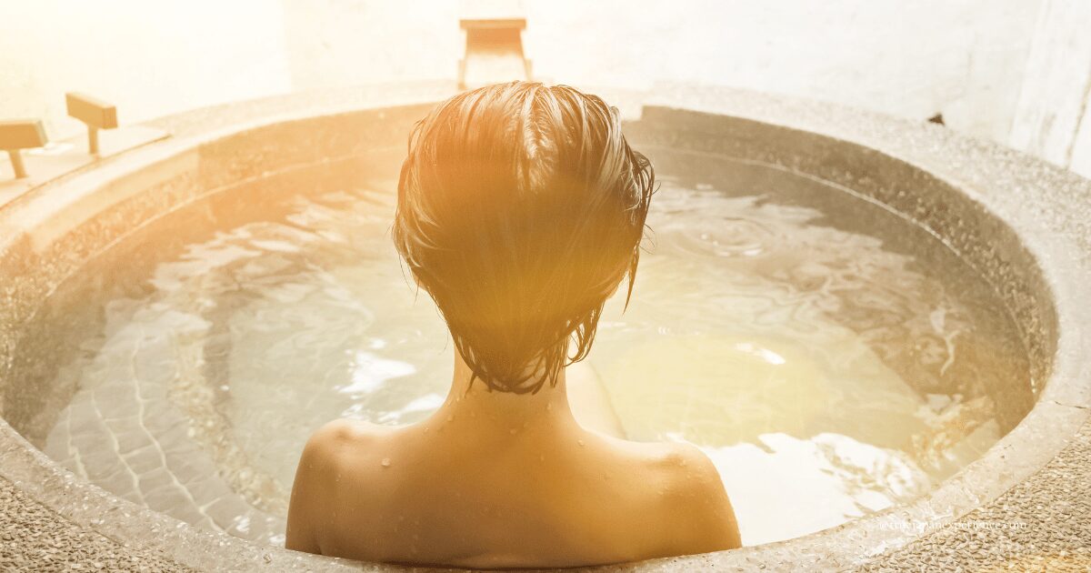 A person enjoying a private hot spring bath alone, with warm sunlight and gentle steam rising from the water.