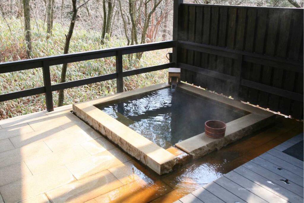 Private outdoor hot spring bath with a wooden bucket and forest view