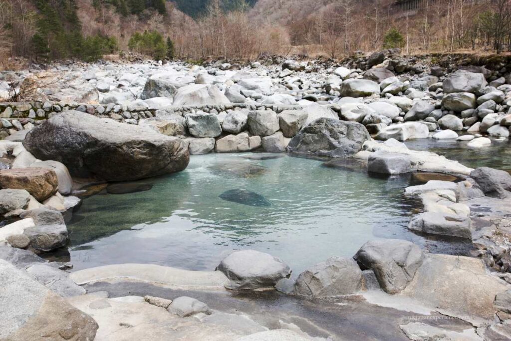 A natural outdoor hot spring surrounded by rocks and mountains, with clear water in a quiet riverside setting in Japan.