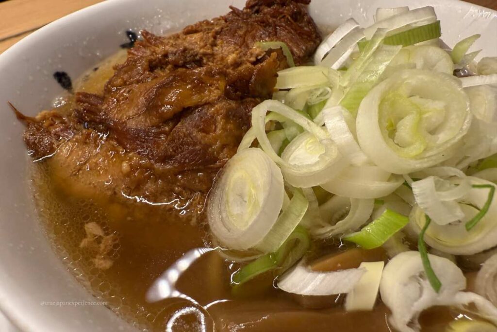A close-up of a bowl of Japanese ramen topped with thick braised pork and sliced green onions in a rich soy-based broth.
