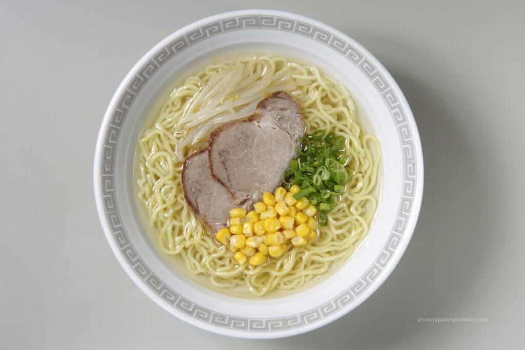 A bowl of Japanese salt ramen topped with sliced pork, sweet corn, green onions, and bean sprouts, viewed from above.