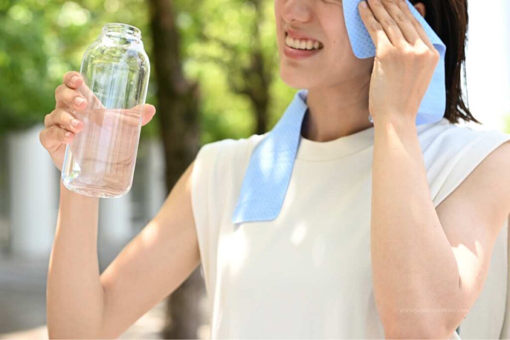 Woman wiping sweat with a towel and holding a water bottle while staying cool in the summer heat.