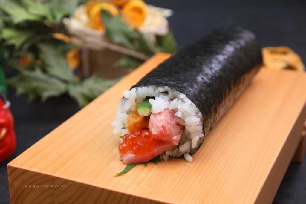 A thick rolled sushi (makizushi) placed on a wooden board, filled with tuna, salmon roe, sea urchin, and other ingredients, wrapped in nori seaweed.