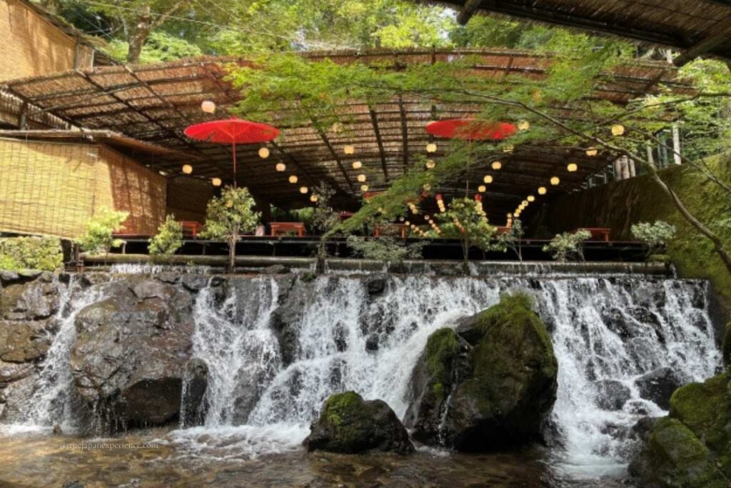 Traditional kawadoko dining platform set above a waterfall along the Kibune River, with red umbrellas and lanterns in summer.