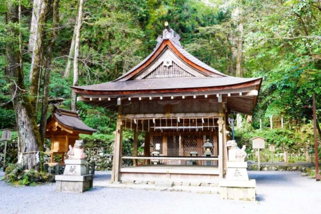 Front view of the main worship hall at Kifune Shrine, surrounded by tall trees and forest, with guardian statues at the entrance.