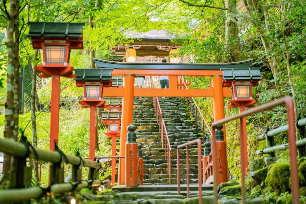 Stone steps leading to a red torii gate and lantern-lined path at Kifune Shrine, surrounded by lush green forest.
