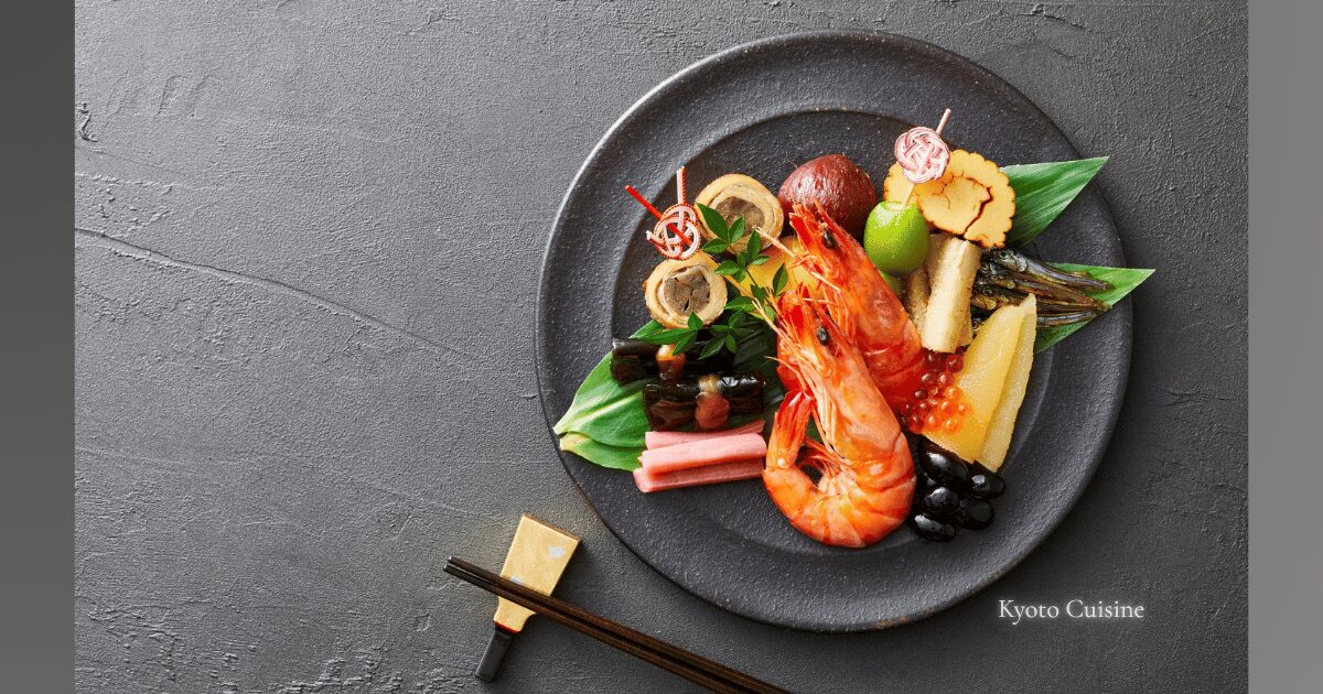 A beautifully arranged Kyoto-style cuisine plate featuring seasonal ingredients like shrimp, rolled omelet, black beans, and pickled vegetables on a dark ceramic dish.
