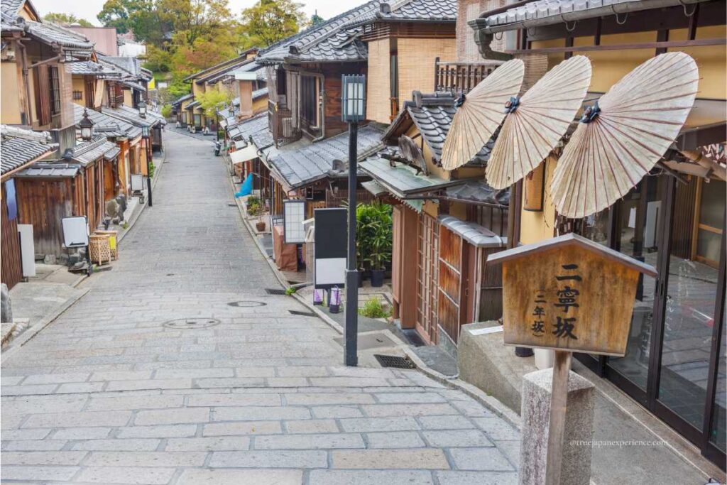 A quiet morning view of Ninenzaka, a historic stone-paved street in Kyoto lined with traditional wooden buildings and Japanese umbrellas.