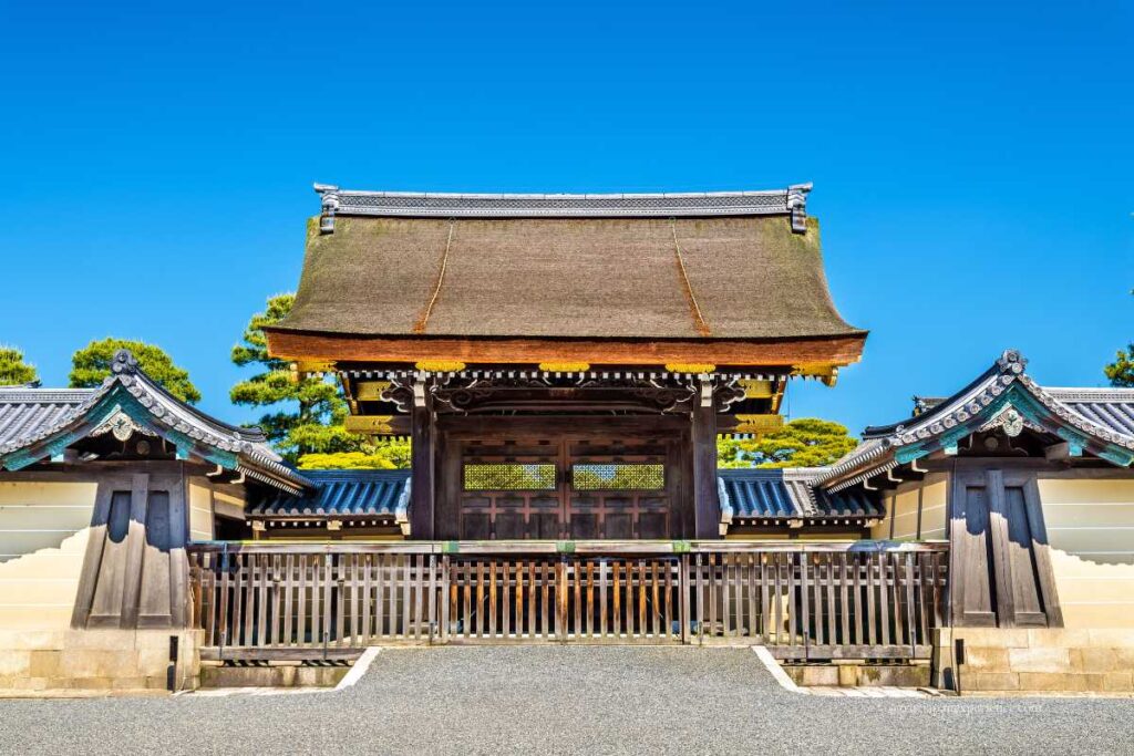 The main wooden gate of Kyoto Imperial Palace, showcasing traditional Japanese architecture with a thatched roof under a clear blue sky.