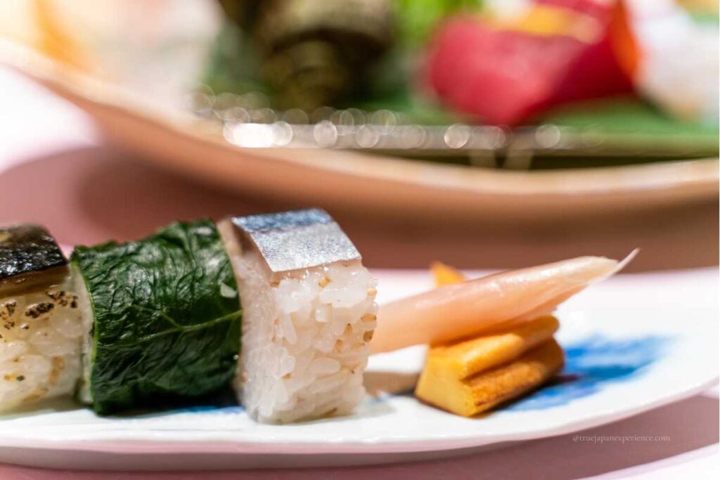 Close-up of traditional Kyoto-style sushi, including mackerel and pickled ginger, elegantly plated on a white dish.