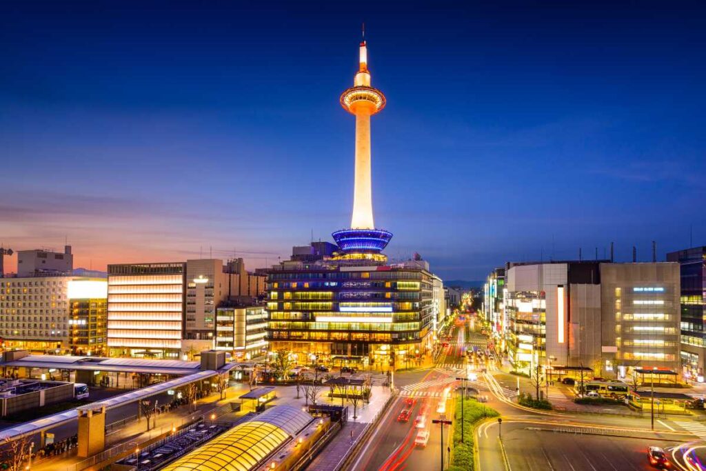 Kyoto Tower illuminated at night, overlooking the cityscape and busy streets near Kyoto Station in central Kyoto.