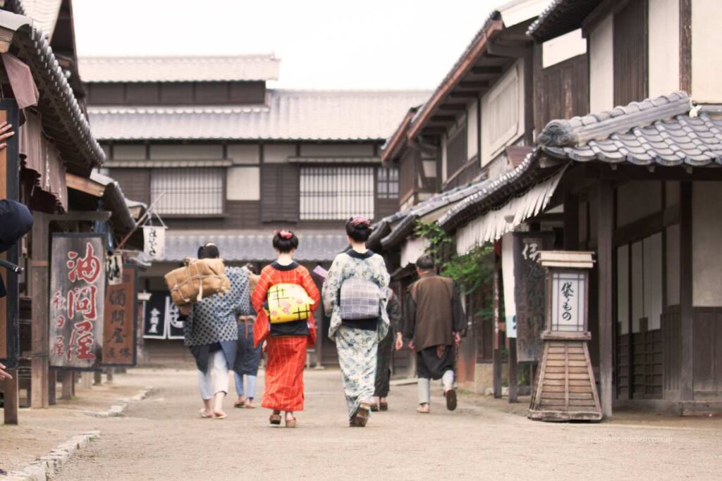 People dressed in kimono walking down a recreated Edo-period street in a historical drama set in Japan.