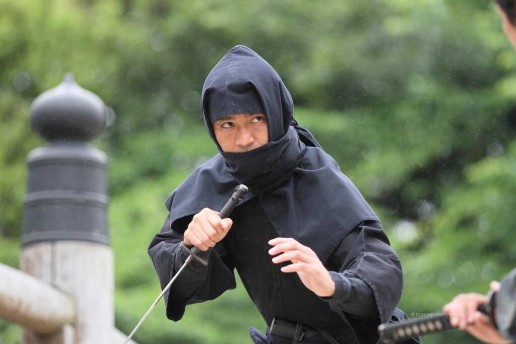 Man dressed as a ninja holding a sword during a performance.