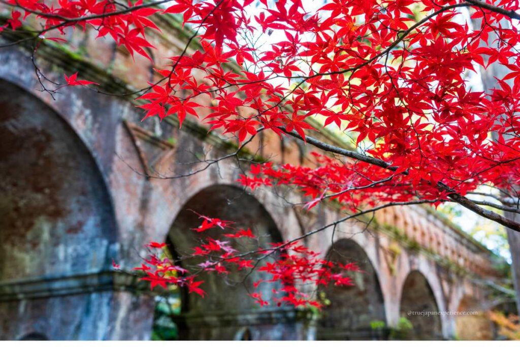 Bright red autumn maple leaves in front of the brick arches of the Suirokaku Aqueduct at Nanzen-ji Temple, Kyoto.