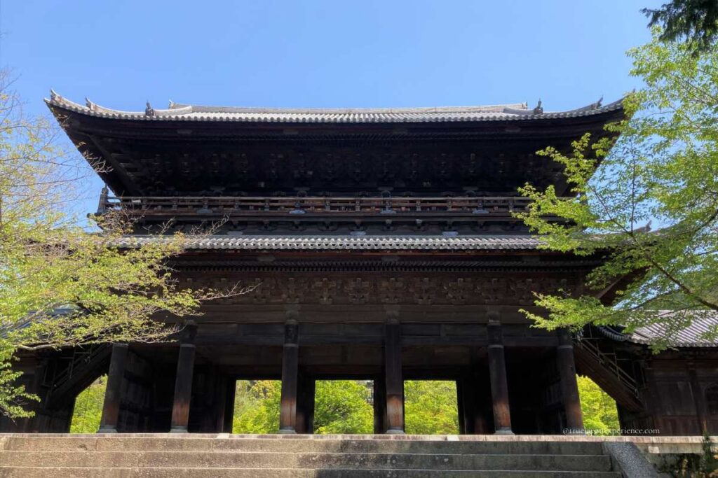 Front view of the massive Sanmon Gate at Nanzen-ji Temple, framed by fresh green maple leaves under a clear blue sky.