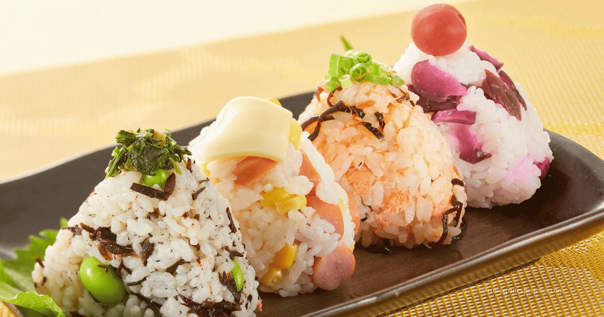 Four colorful onigiri rice balls with various fillings, neatly arranged on a black plate. Each onigiri features different ingredients like seaweed, vegetables, and pickled plum, showcasing the variety and appeal of Japanese rice balls.