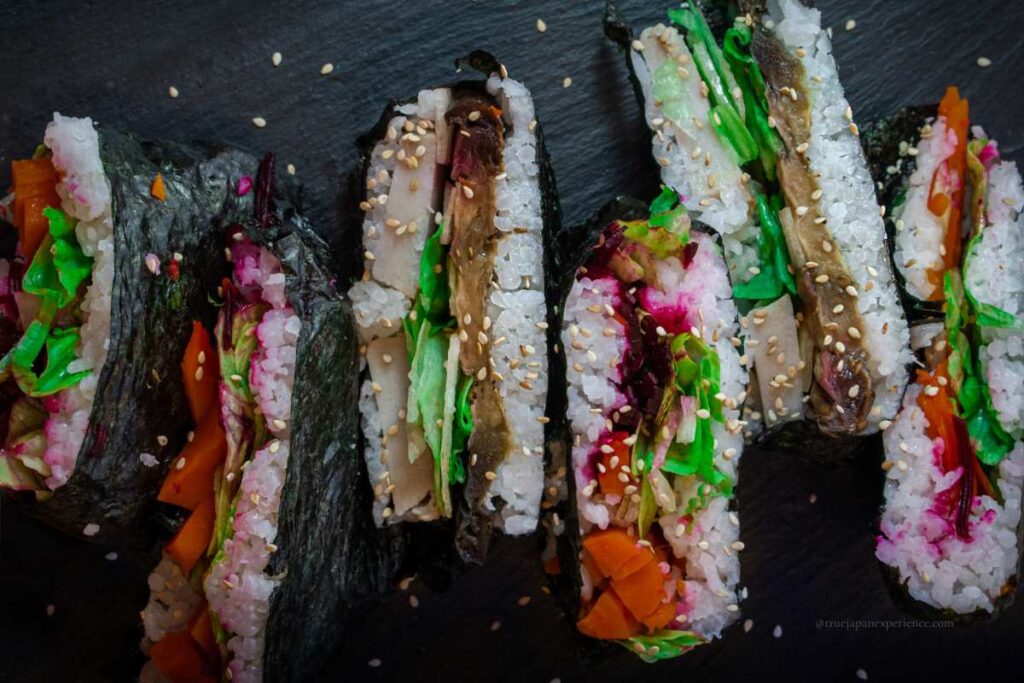 Colorful onigirazu filled with vegetables and wrapped in seaweed, topped with sesame seeds.