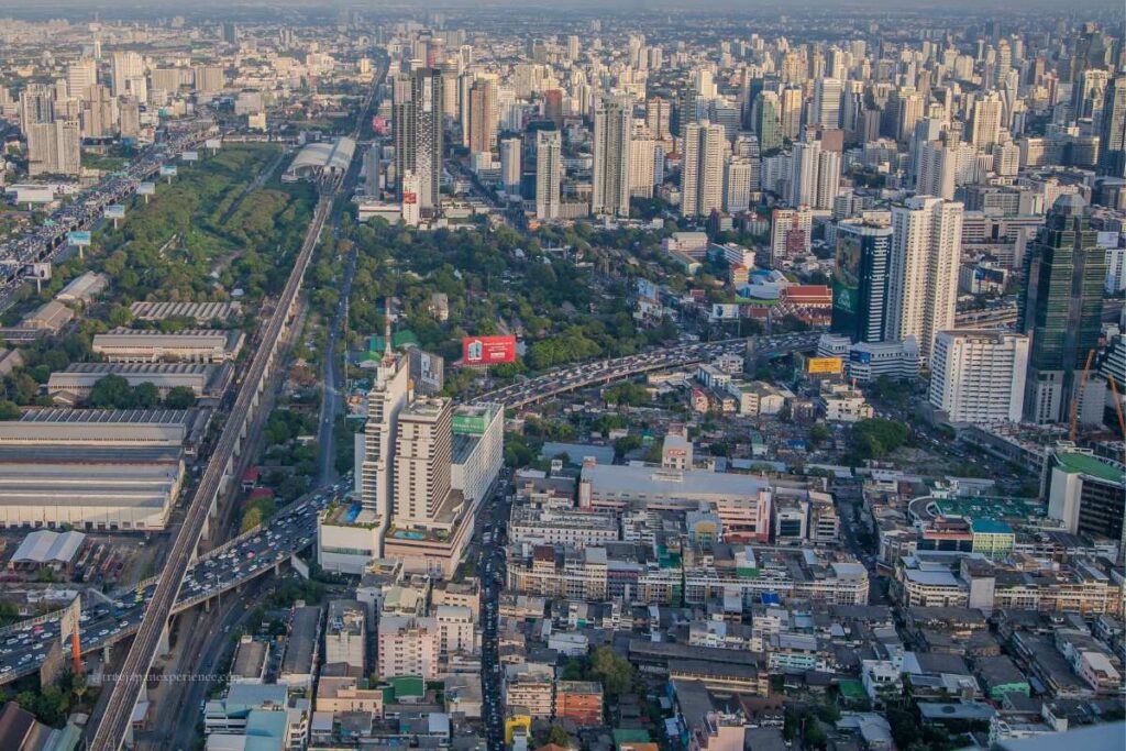 Aerial view of a densely populated city with high-rise buildings, green parks, elevated highways, and a central train station.