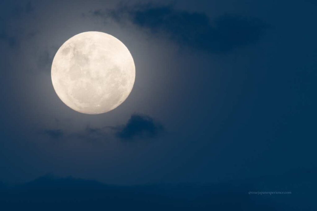 A bright full moon glowing in the night sky, partially surrounded by soft clouds.