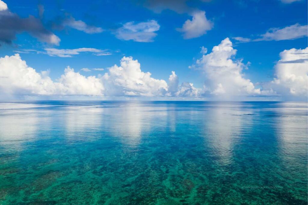 The crystal-clear turquoise sea of Ishigaki Island, Okinawa, reflecting the blue sky and white clouds on a calm summer day.