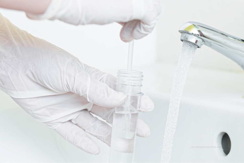A person wearing gloves collecting tap water into a test tube for quality inspection.